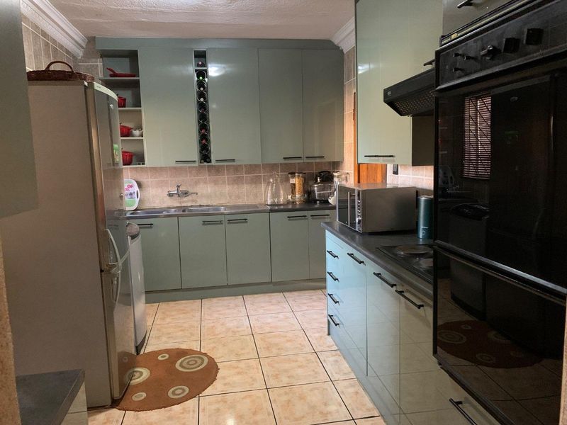 A functional kitchen featuring light green cabinetry, tiled backsplash, built-in oven, hob, and extractor fan with tiled flooring throughout.