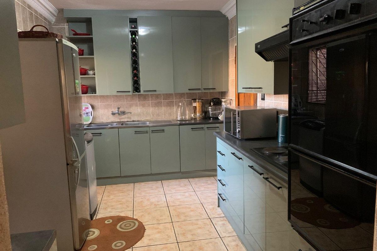 A functional kitchen featuring light green cabinetry, tiled backsplash, built-in oven, hob, and extractor fan with tiled flooring throughout.