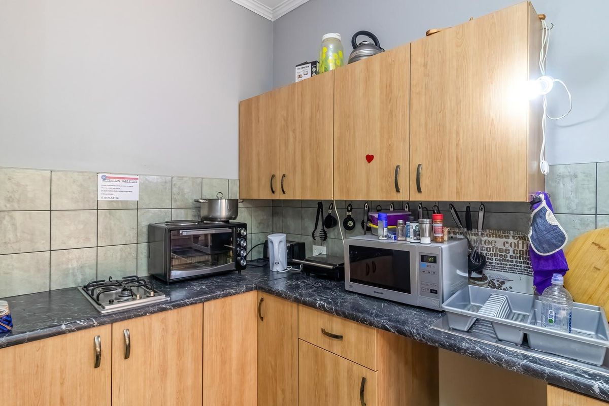 A functional kitchen area featuring light wood-finish cabinetry, dark laminate countertops, a gas hob, and tiled backsplash.