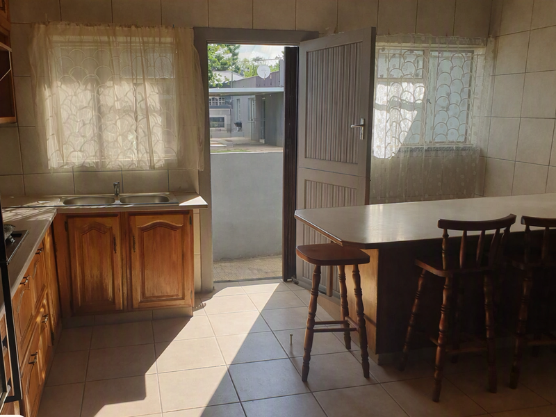 A functional kitchen featuring wooden cabinetry, a double sink, tiled surfaces, and a breakfast bar with direct access to the exterior.