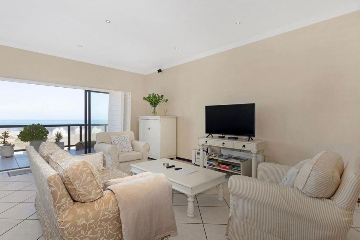 A bright living room featuring tiled flooring, recessed ceiling lighting, and large sliding glass doors opening onto a balcony with ocean views.