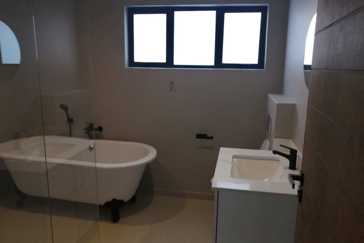 Modern bathroom featuring a freestanding clawfoot bathtub, a contemporary vanity with a stone countertop, and dark matte fixtures.