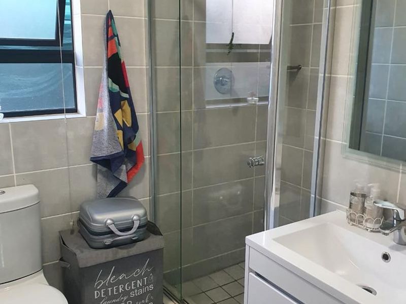 A modern bathroom featuring a glass-enclosed shower, a wall-mounted vanity with a basin, and neutral wall tiling.