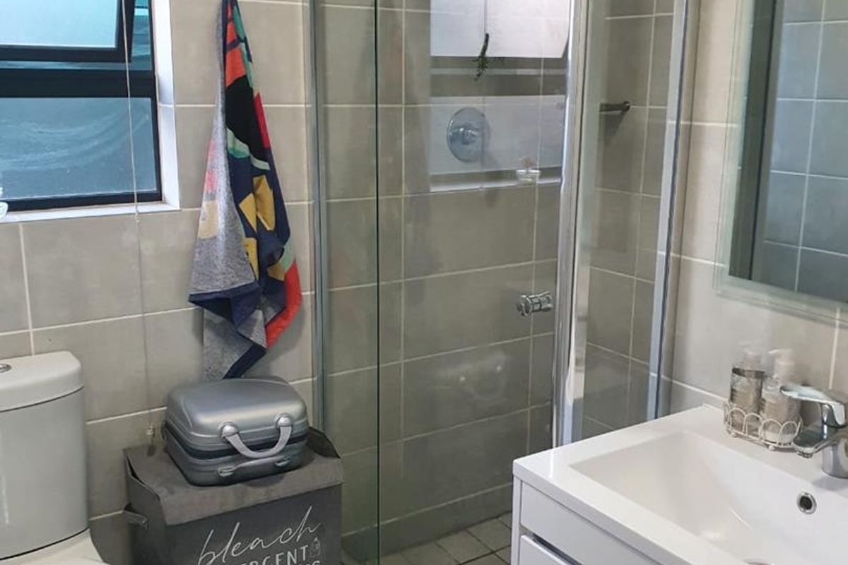 A modern bathroom featuring a glass-enclosed shower, a wall-mounted vanity with a basin, and neutral wall tiling.