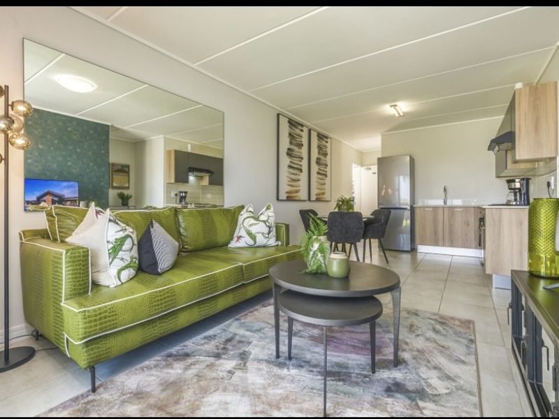 An open-plan living and kitchen area featuring tiled flooring, modern cabinetry, and a large feature mirror, creating a bright and functional living space.
