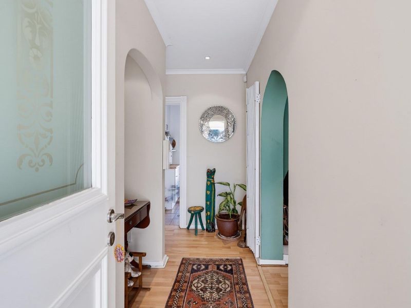 A bright and welcoming hallway featuring timber flooring, arched architectural details, and recessed lighting, providing access to adjoining living spaces.