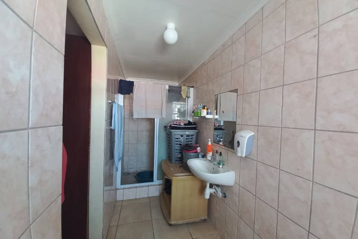 A functional bathroom featuring wall-to-wall tiling, a wall-mounted basin, and a shower enclosure with a glass door.