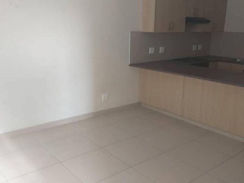 A clean, empty kitchen featuring light wood-finish cabinetry, laminate countertops, and tiled flooring, offering a functional and neutral space ready for personalization.