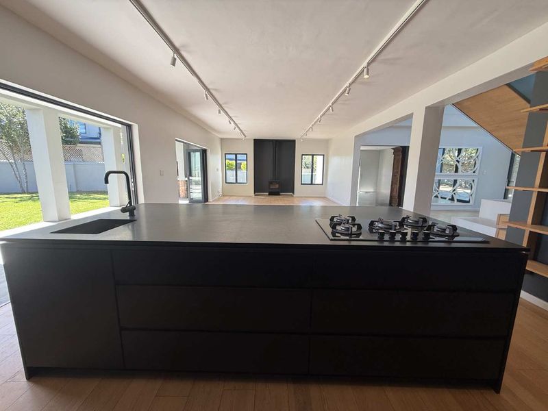 Spacious open-plan living area featuring a large modern kitchen island with integrated gas cooktop, hardwood floors, and a fireplace, opening onto a garden.