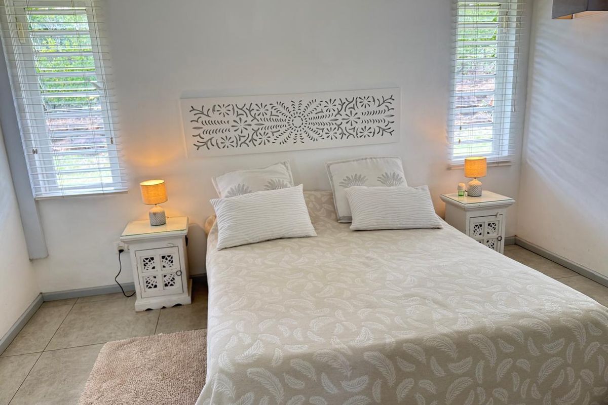 A bright and well-maintained bedroom featuring tiled flooring, dual windows with fitted blinds, and a decorative wall-mounted headboard panel.