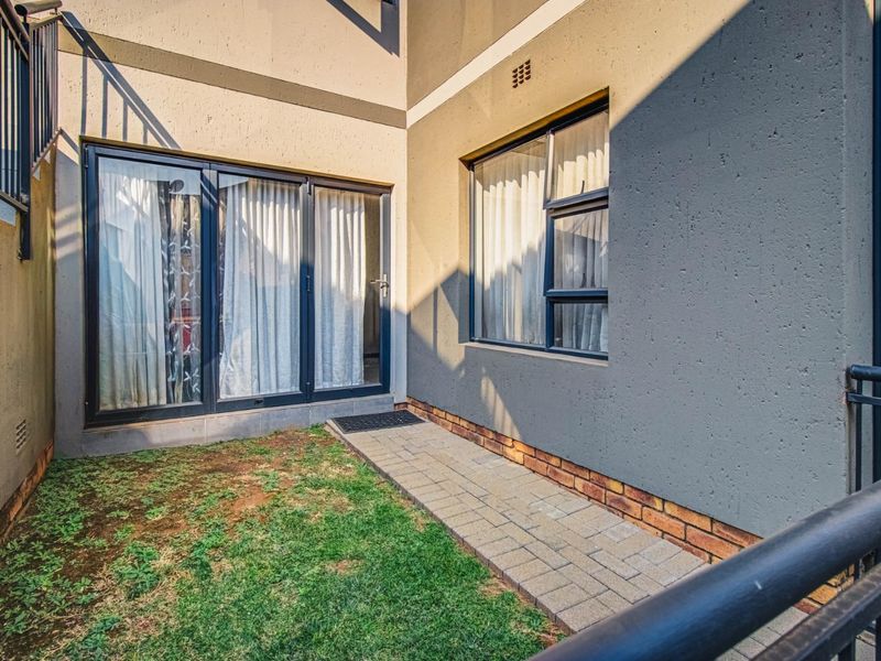 A rear exterior view of the townhouse featuring a paved walkway, small lawn area, and modern aluminium framed doors and windows.