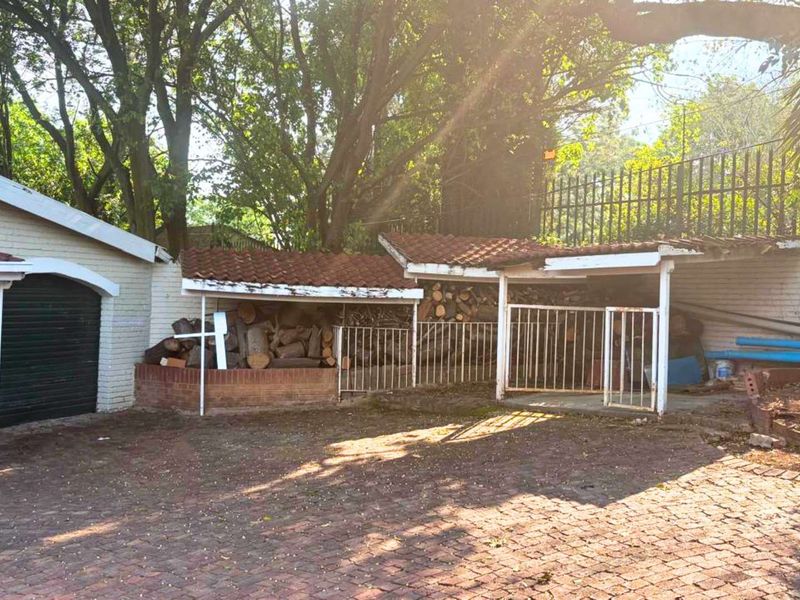 Rear exterior area featuring a brick-paved driveway, covered storage structures with tiled roofing, and perimeter security fencing.