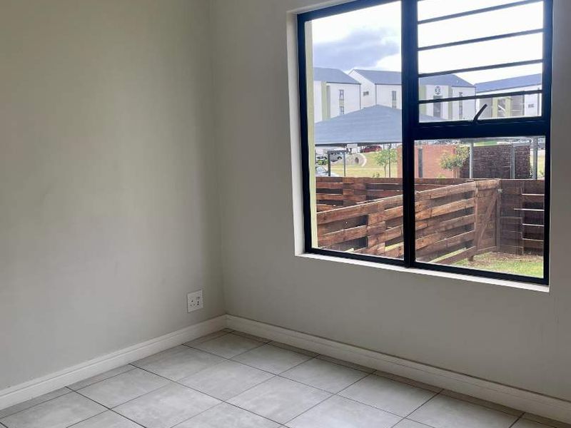 A clean, empty bedroom featuring neutral tiled flooring, a pendant light, and a window fitted with security bars.