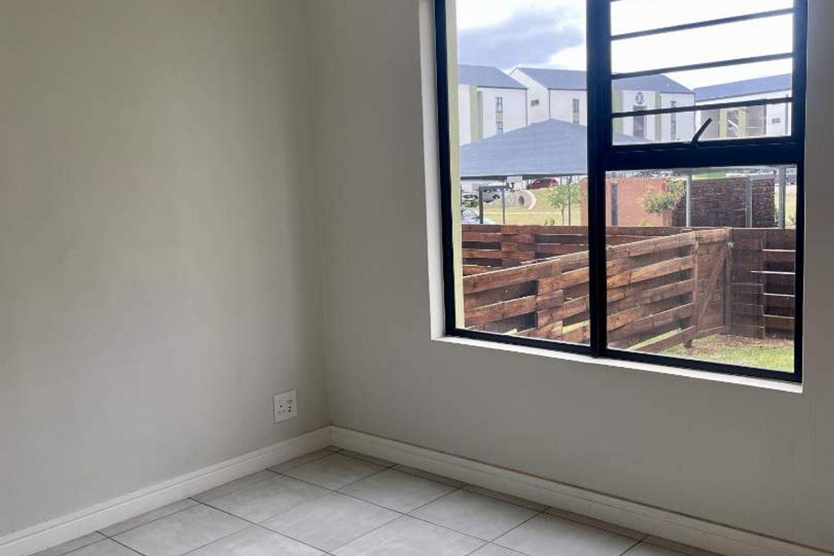 A clean, empty bedroom featuring neutral tiled flooring, a pendant light, and a window fitted with security bars.