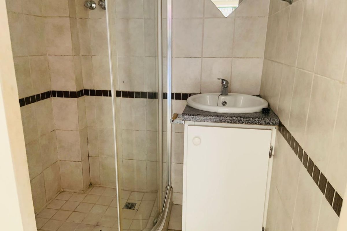 Compact bathroom featuring a corner glass shower enclosure, a vanity with a drop-in basin, and tiled walls with a decorative border.