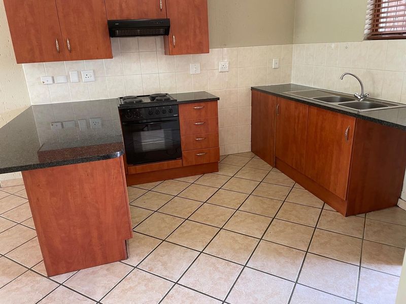 A functional kitchen featuring wooden cabinetry, granite countertops, a built-in oven with hob, extractor fan, and tiled flooring.