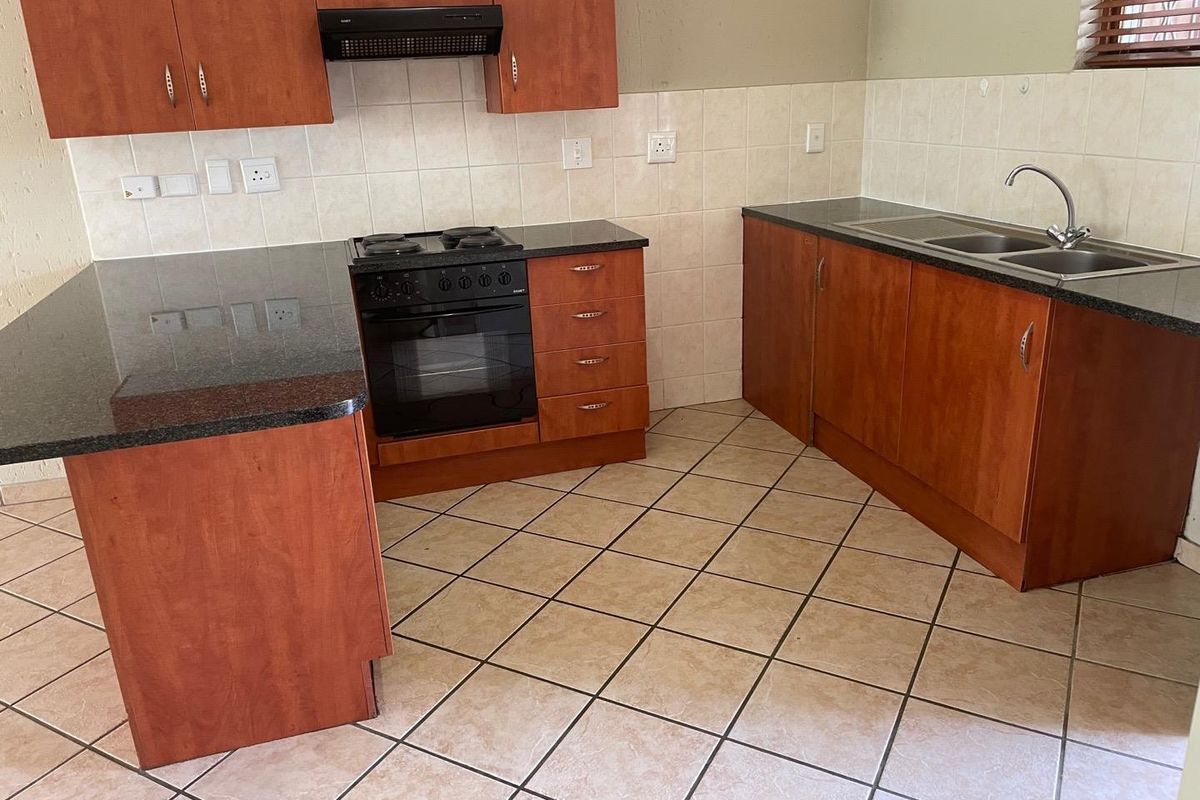 A functional kitchen featuring wooden cabinetry, granite countertops, a built-in oven with hob, extractor fan, and tiled flooring.