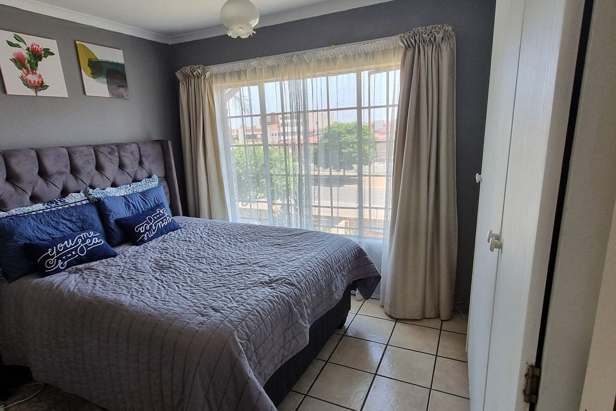A well-maintained bedroom featuring tiled flooring, a built-in wardrobe, and a sliding door with security gate providing natural light.