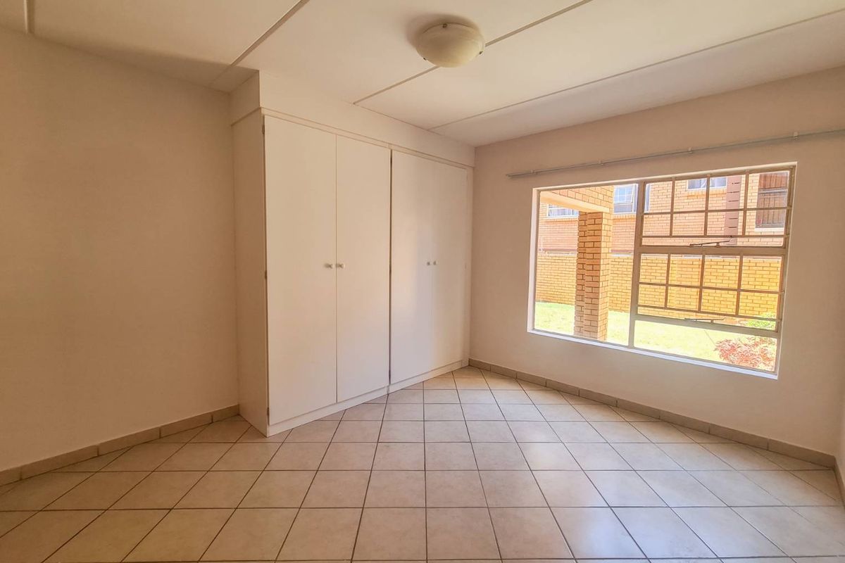 A bright, empty bedroom featuring neutral tiled flooring, built-in cupboards, and a large window providing natural light.