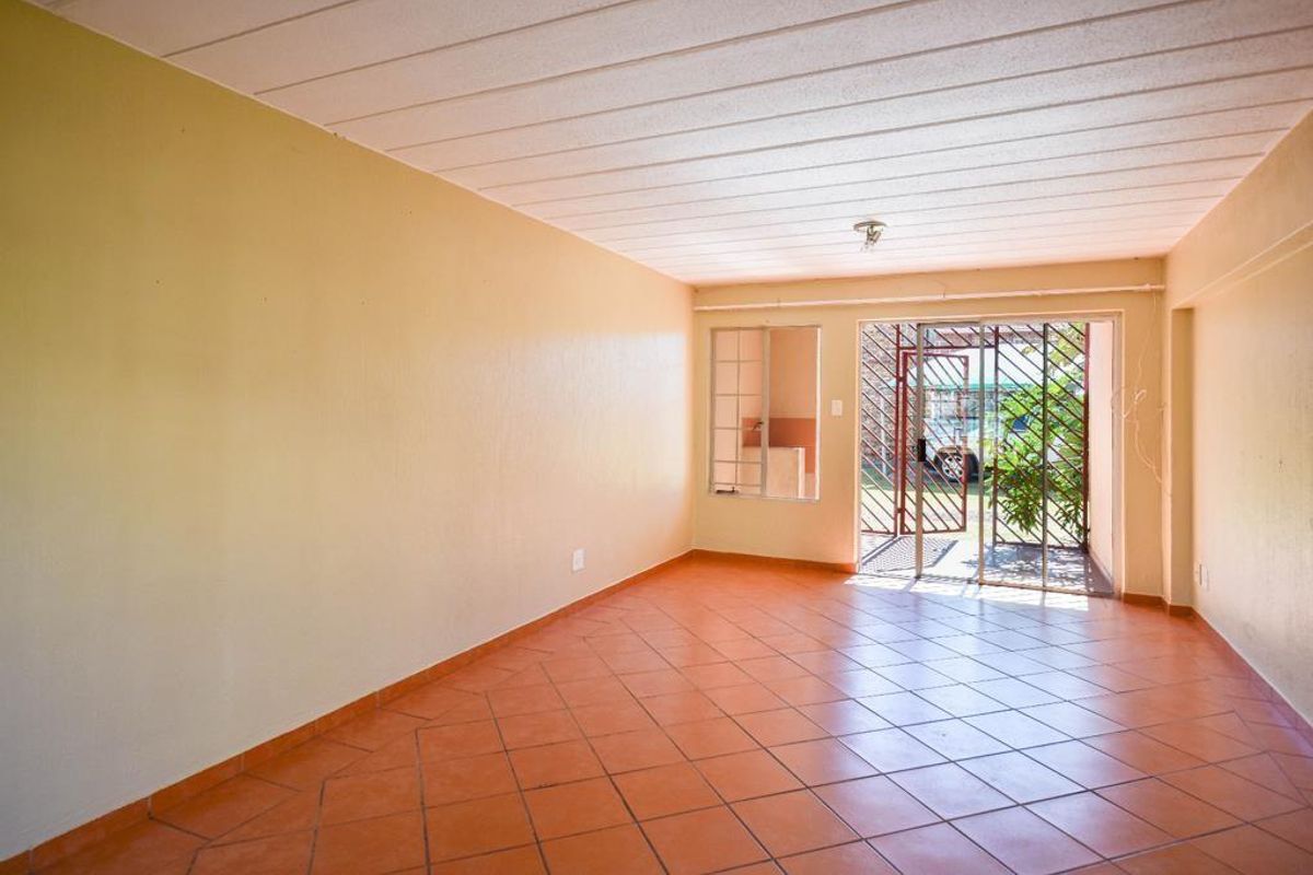 An empty, tiled living area featuring a sliding glass door with a security gate and a panel ceiling.