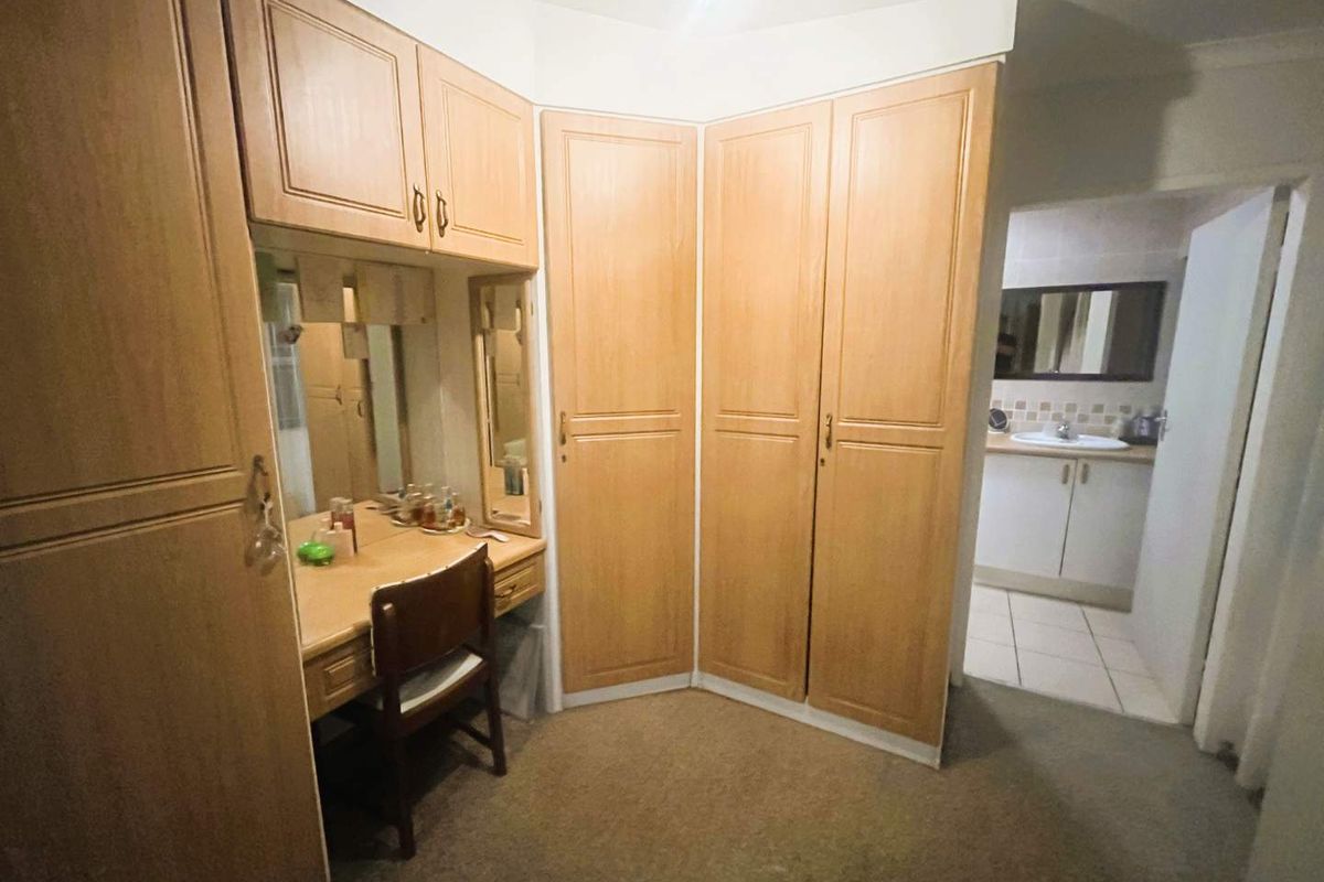Bedroom featuring built-in wooden cabinetry with an integrated vanity station, leading into an en-suite bathroom with tiled flooring.