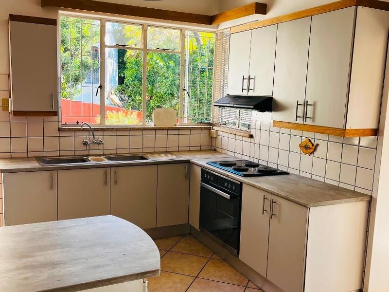 A functional kitchen featuring light-toned cabinetry, laminate countertops, tiled backsplash, and integrated appliances, with natural light from a large window.