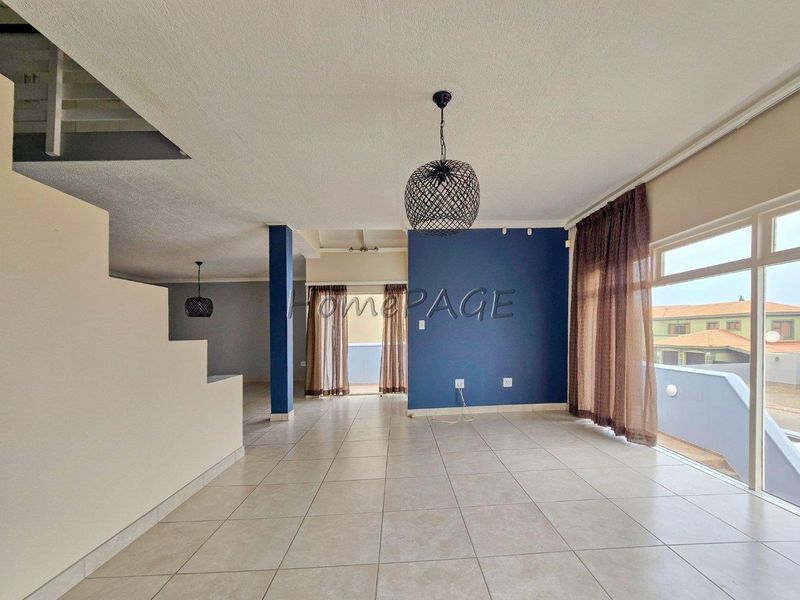 Spacious open-plan living area featuring neutral tiled flooring, a central staircase, and large sliding doors leading to an outdoor balcony.