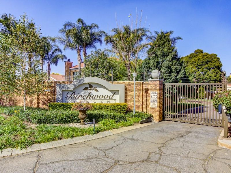 Entrance view of Birchwood Crescent featuring a brick boundary wall, electric fencing, and a secure metal gate leading into the complex.