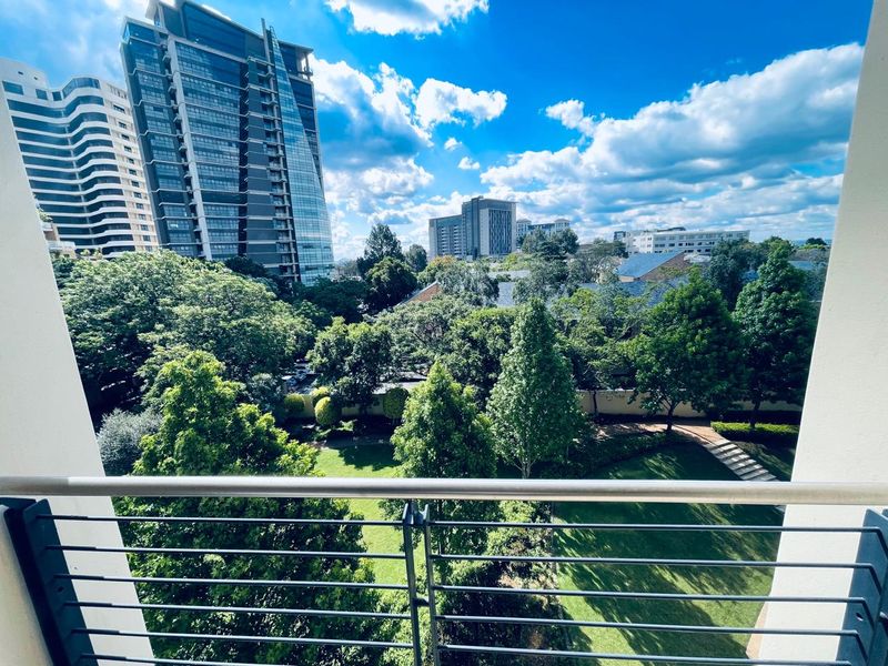 Elevated urban view overlooking lush green gardens and surrounding high-rise buildings from a private balcony.