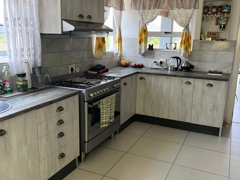 A functional kitchen featuring light wood-grain cabinetry, a gas stove with extractor fan, tiled backsplash, and neutral floor tiles.