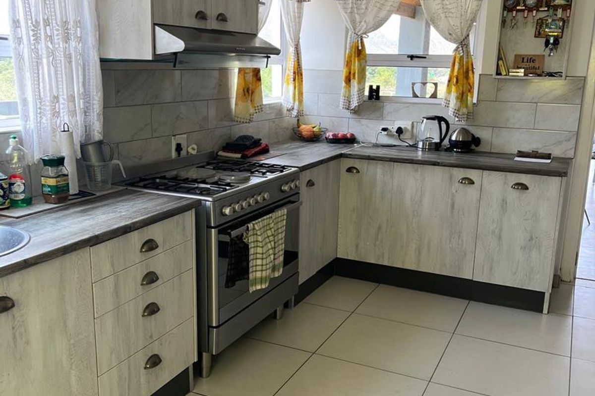 A functional kitchen featuring light wood-grain cabinetry, a gas stove with extractor fan, tiled backsplash, and neutral floor tiles.