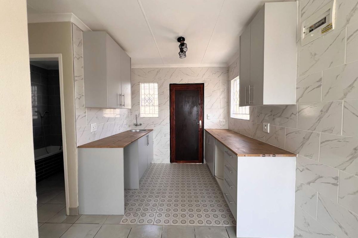 A clean, modern kitchen featuring light grey cabinetry, wooden countertops, marble-effect wall tiling, and tiled flooring, presented in an empty, move-in ready state.