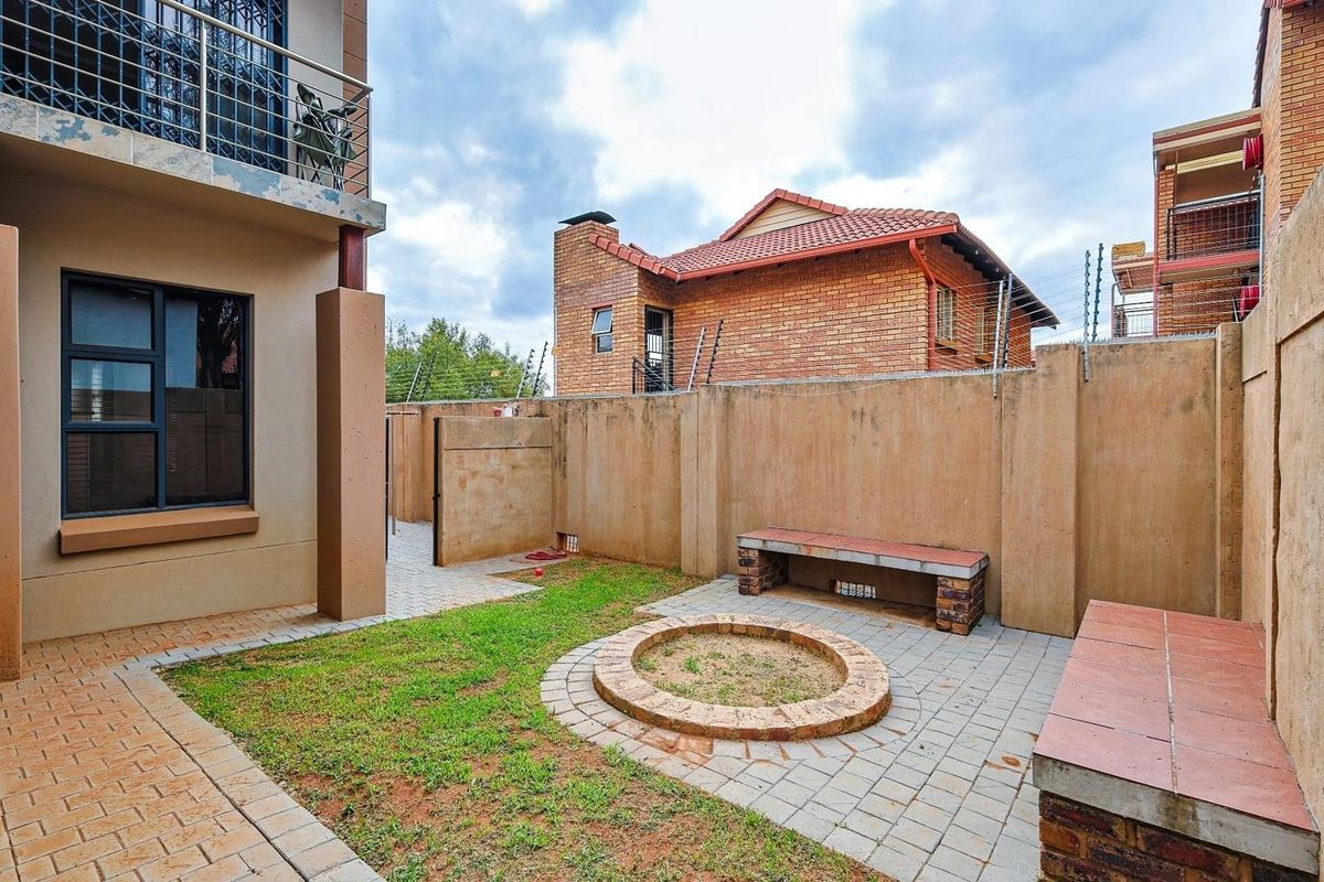 A private rear courtyard featuring a paved area with a built-in fire pit, brick seating, and a small lawn section enclosed by high boundary walls.