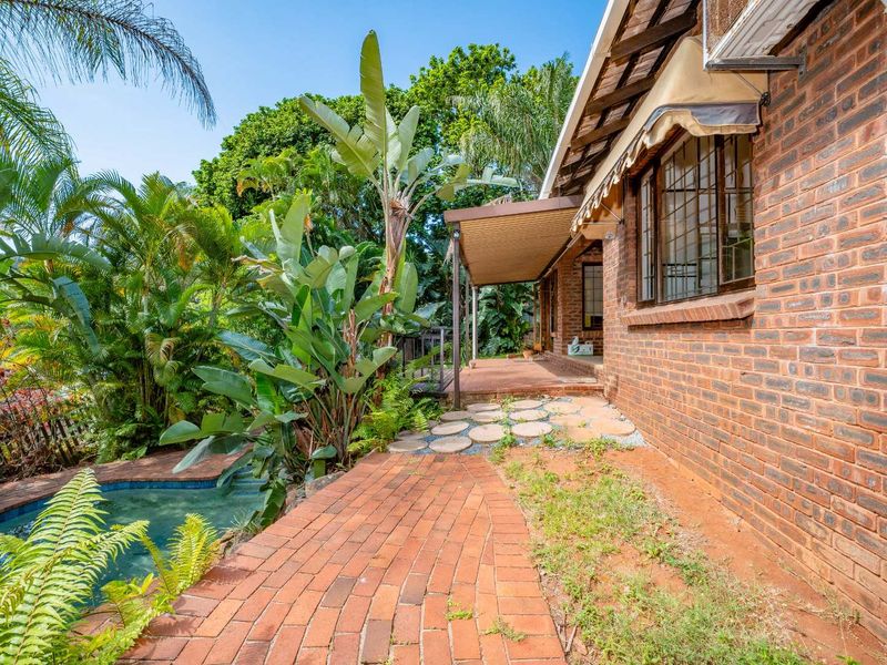 Rear exterior view featuring a brick facade, covered patio area, and an adjacent swimming pool surrounded by established garden landscaping.
