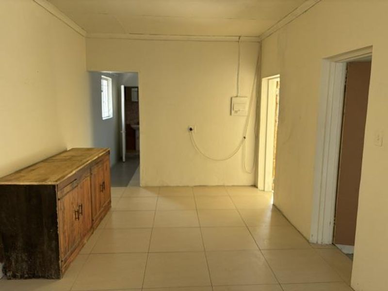 An empty living area featuring tiled flooring and coving, with visible wall staining and exposed electrical wiring requiring attention.