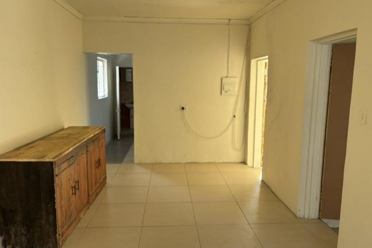 An empty living area featuring tiled flooring and coving, with visible wall staining and exposed electrical wiring requiring attention.