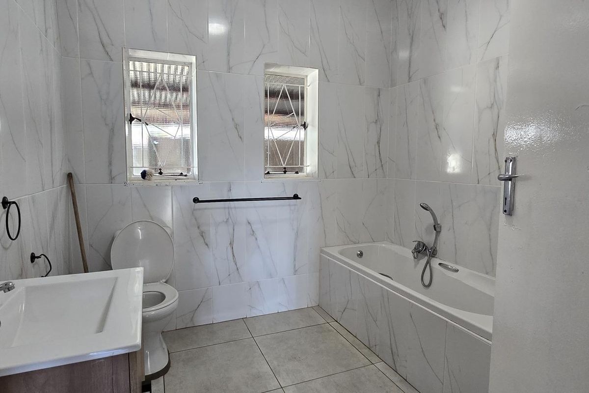 A modern bathroom featuring marble-look wall tiles, a built-in bathtub, a vanity basin, and a toilet, with security bars on the windows.