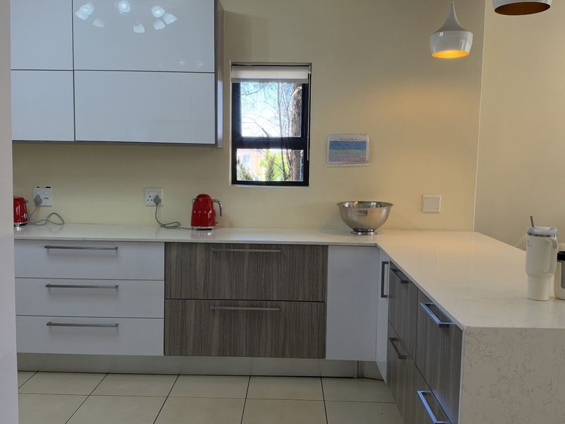 Modern kitchen featuring high-gloss and wood-grain cabinetry, quartz countertops, and tiled flooring, offering a clean and contemporary aesthetic.