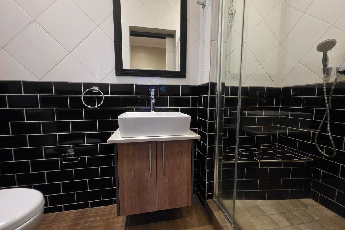 Modern bathroom featuring a vessel sink on a wood-finish vanity, a glass-enclosed shower with a built-in tiled bench, and contrasting black and white wall tiles.