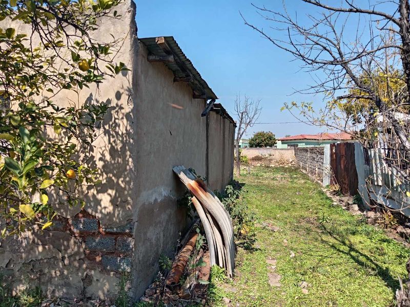 Rear exterior view of the property showing a weathered masonry wall with significant plaster damage and a corrugated metal roof structure.