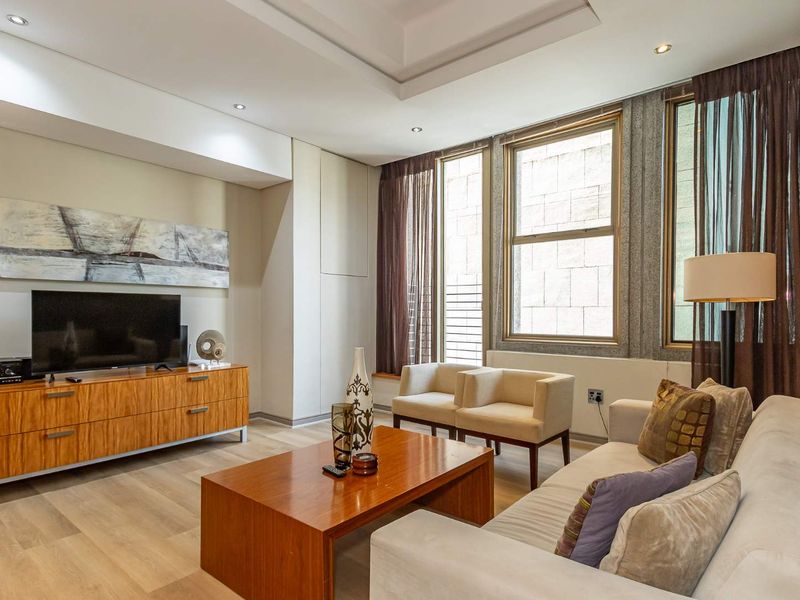A well-lit living room featuring a tray ceiling, recessed lighting, and large windows with modern laminate flooring.