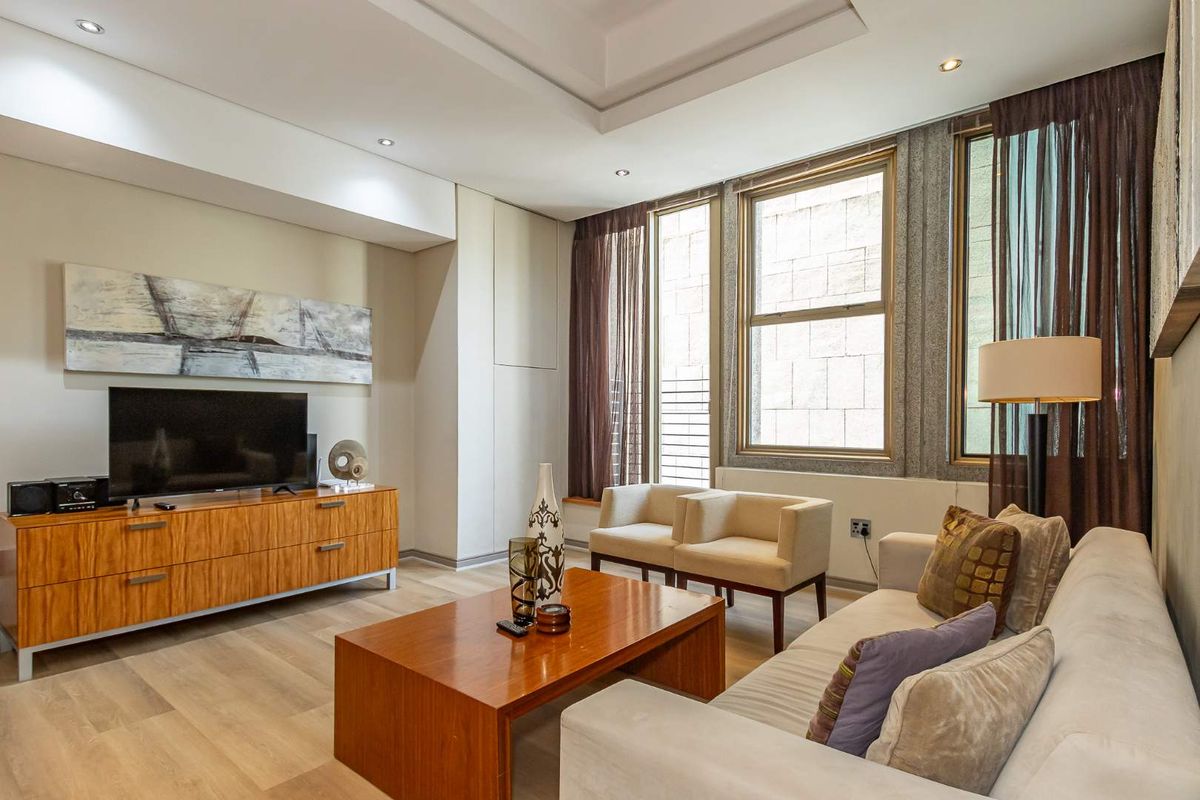 A well-lit living room featuring a tray ceiling, recessed lighting, and large windows with modern laminate flooring.