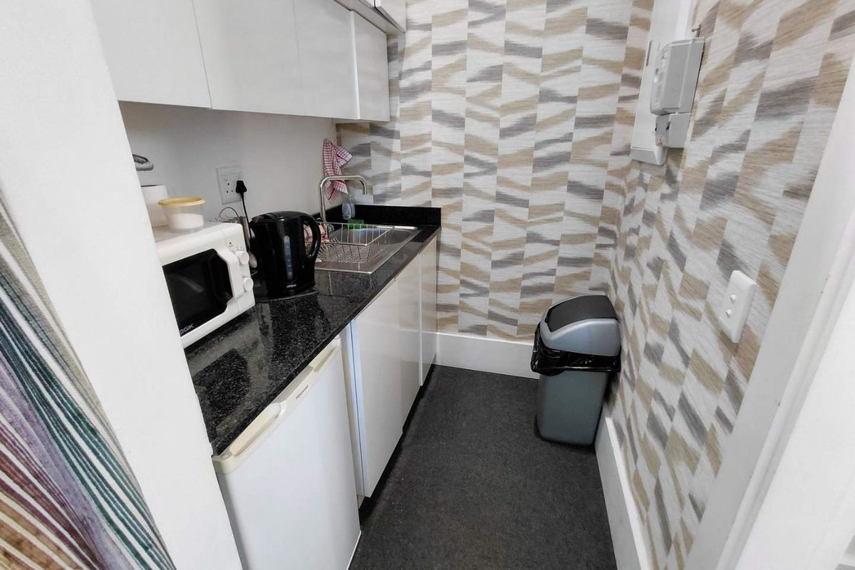 Compact scullery area featuring white cabinetry, granite countertops, a stainless steel sink, and decorative patterned wallpaper.