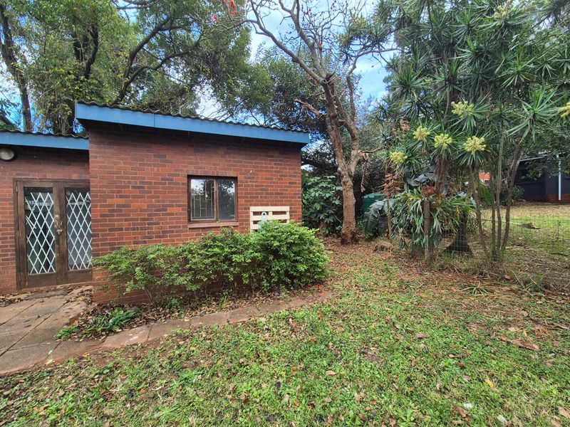 A view of the rear brick exterior of the house, featuring a security gate, window with bars, and surrounding garden area.