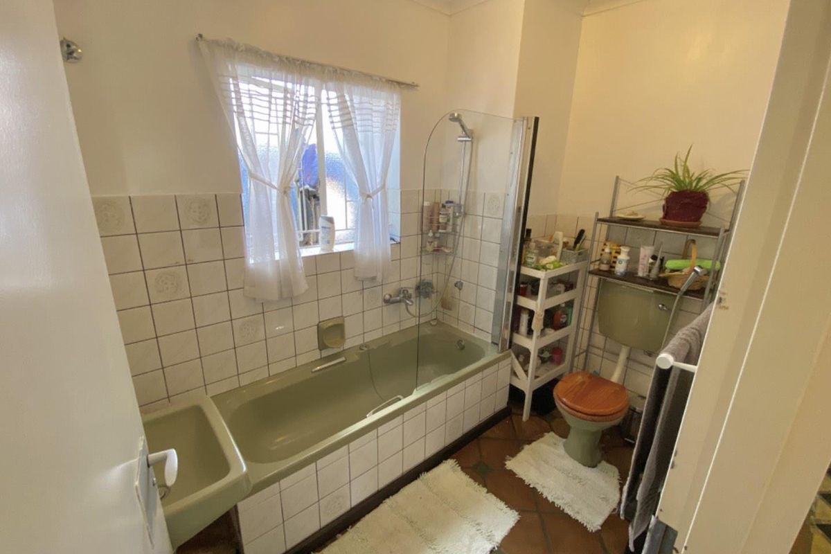 A dated bathroom featuring a vintage green bathtub and toilet suite, tiled splashbacks, and a glass shower screen over the bath.