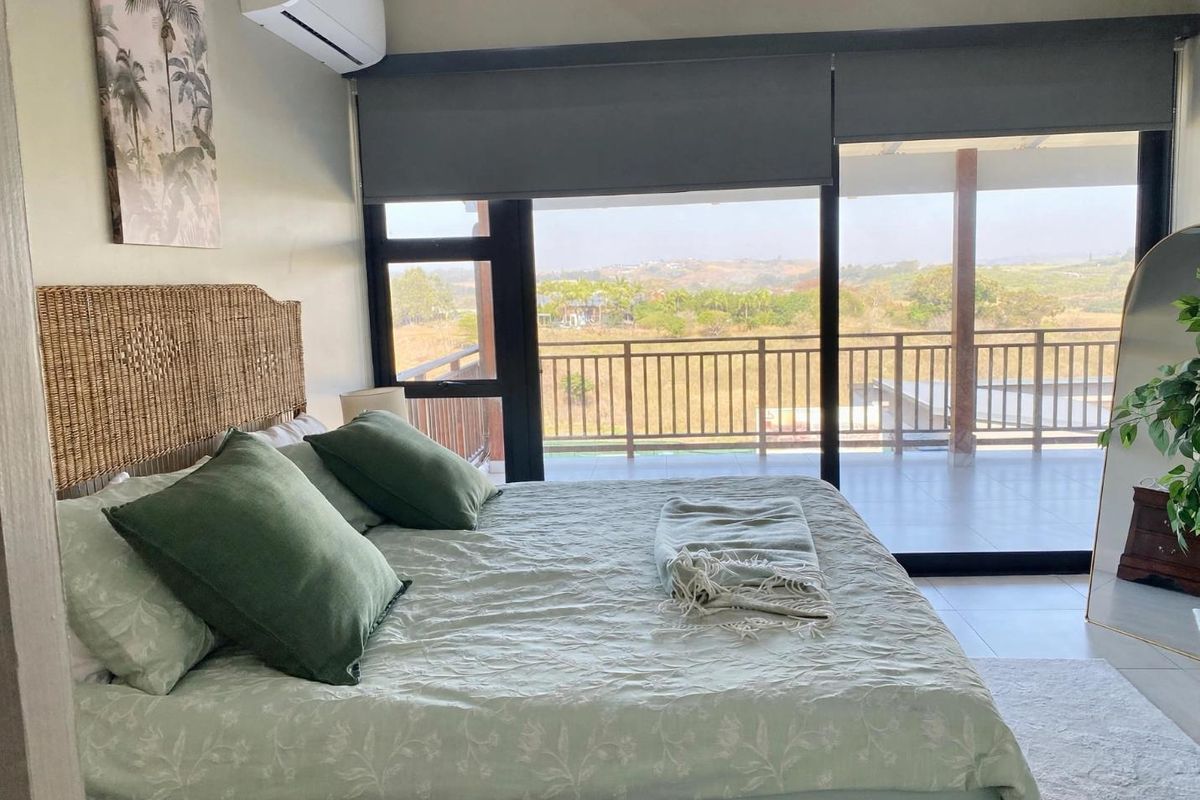 A well-maintained bedroom featuring tiled flooring, a split-system air conditioner, and large sliding glass doors that open onto a balcony with scenic views.