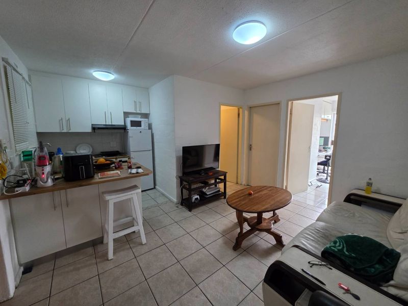 Open-plan living area featuring a compact kitchen with built-in cabinetry and tiled flooring throughout, providing a functional and connected living space.