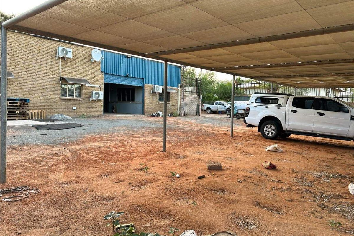 Rear exterior area featuring a large shade cloth carport structure, brick building facade, and metal roller door access.