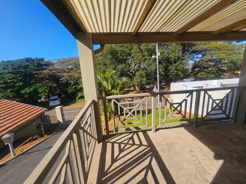 An elevated balcony featuring a corrugated roof, timber balustrades, and concrete flooring, offering an outdoor space with views of the surrounding property.