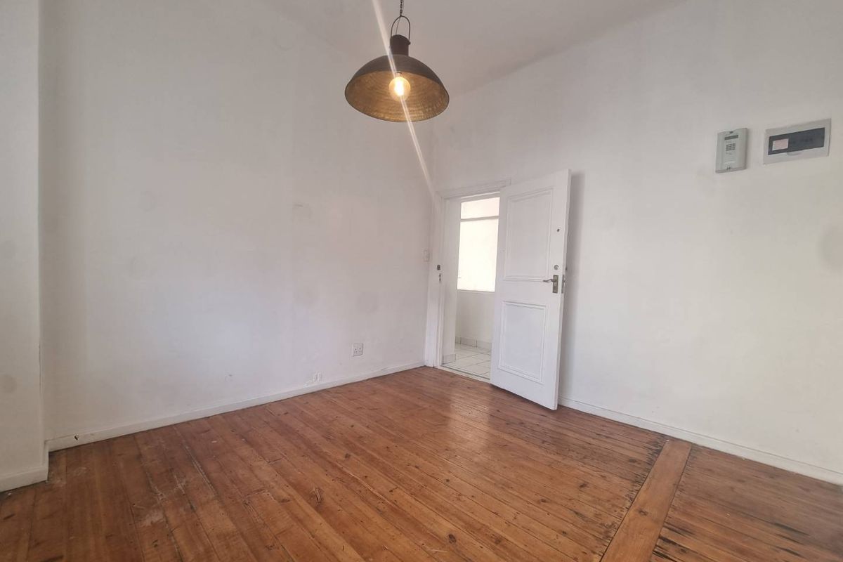 An empty bedroom featuring original hardwood flooring, a pendant light fixture, and neutral walls, offering a blank canvas for personalization.